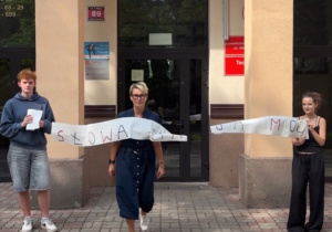 Uczniowie wraz z nauczycielem trzymający rolkę papieru z napisem słowa mają moc