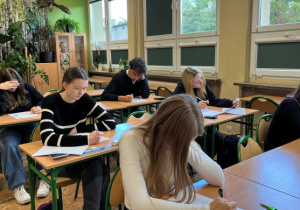 Uczniowie siedzą w ławkach lekcyjnych i rozwiązują test podczas pierwszego etapu eliminacji