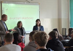 pracownicy US na tle tablicy oraz uczniowie słuchający wykładu