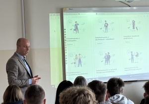 pracownicy US na tle tablicy oraz uczniowie słuchający wykładu