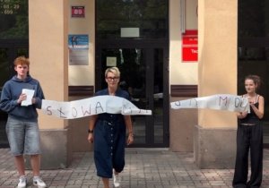 Uczniowie wraz z nauczycielem trzymający rolkę papieru z napisem słowa mają moc