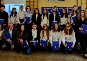 Wręczenie uczniom certyfikatów Europass po zakończeniu projektu Erasmus+. Uczniowie odbierają dokumenty podczas uroczystości.